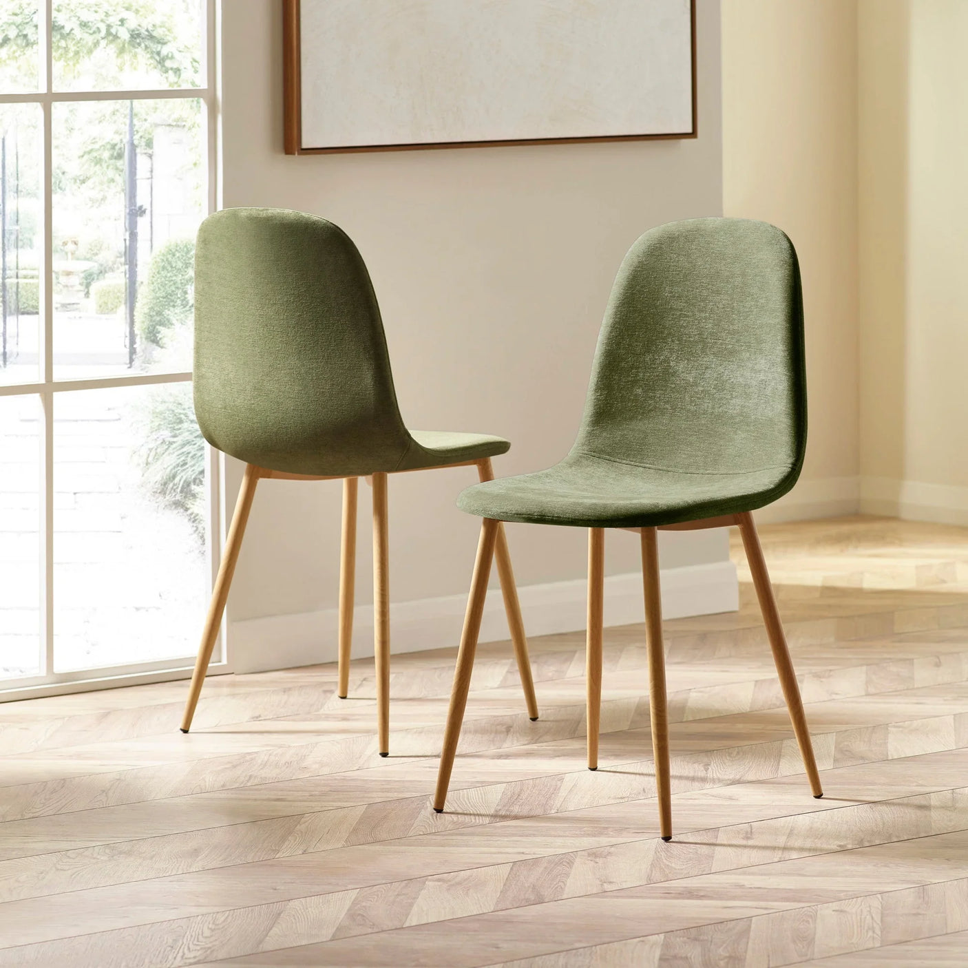 Pair of green velvet dining chairs with wooden legs on herringbone floor in bright room