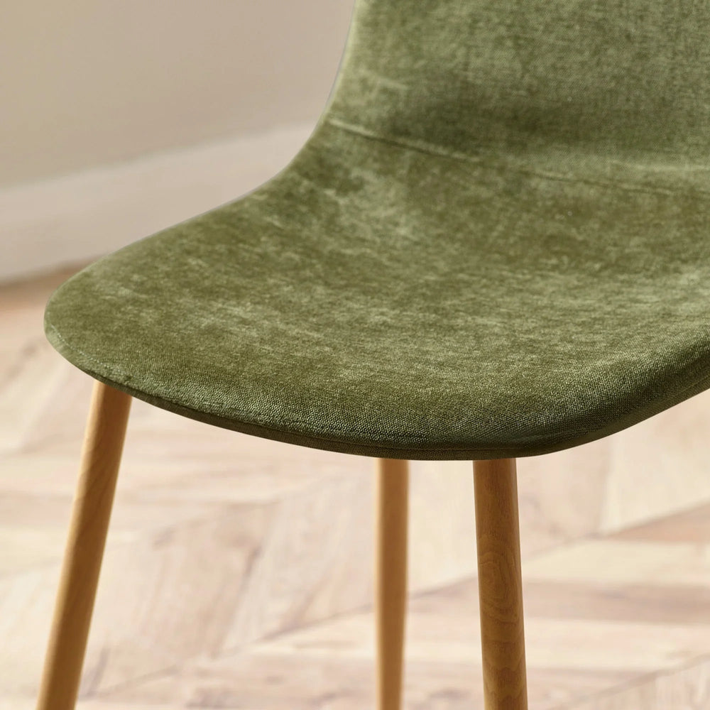 Green velvet dining chair seat with wooden legs on light herringbone floor