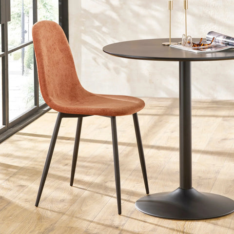 Rust velvet dining chair with black metal legs next to round black dining table on wood floor