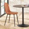 Rust velvet dining chair with black metal legs next to round black dining table on wood floor