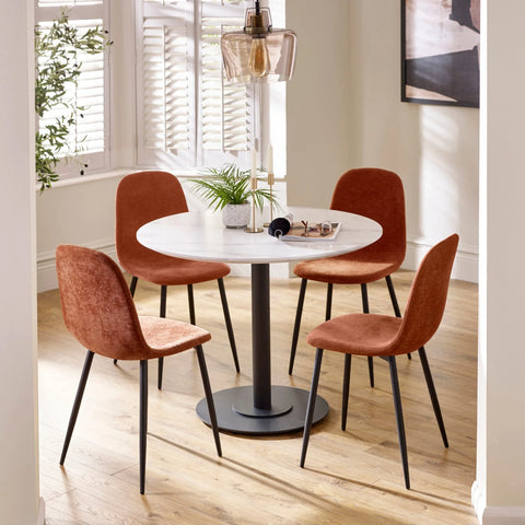 Round dining table with white top and four orange fabric chairs on wood floor