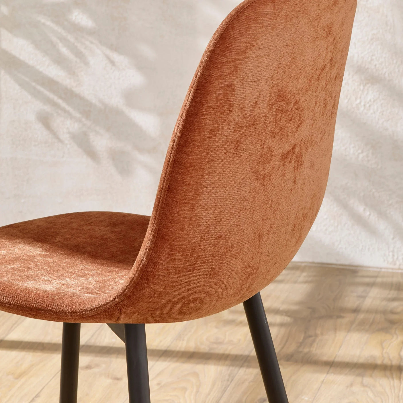 Rust velvet dining chair with black legs on wooden floor, side view