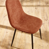Rust velvet dining chair with curved backrest and black legs on wood floor