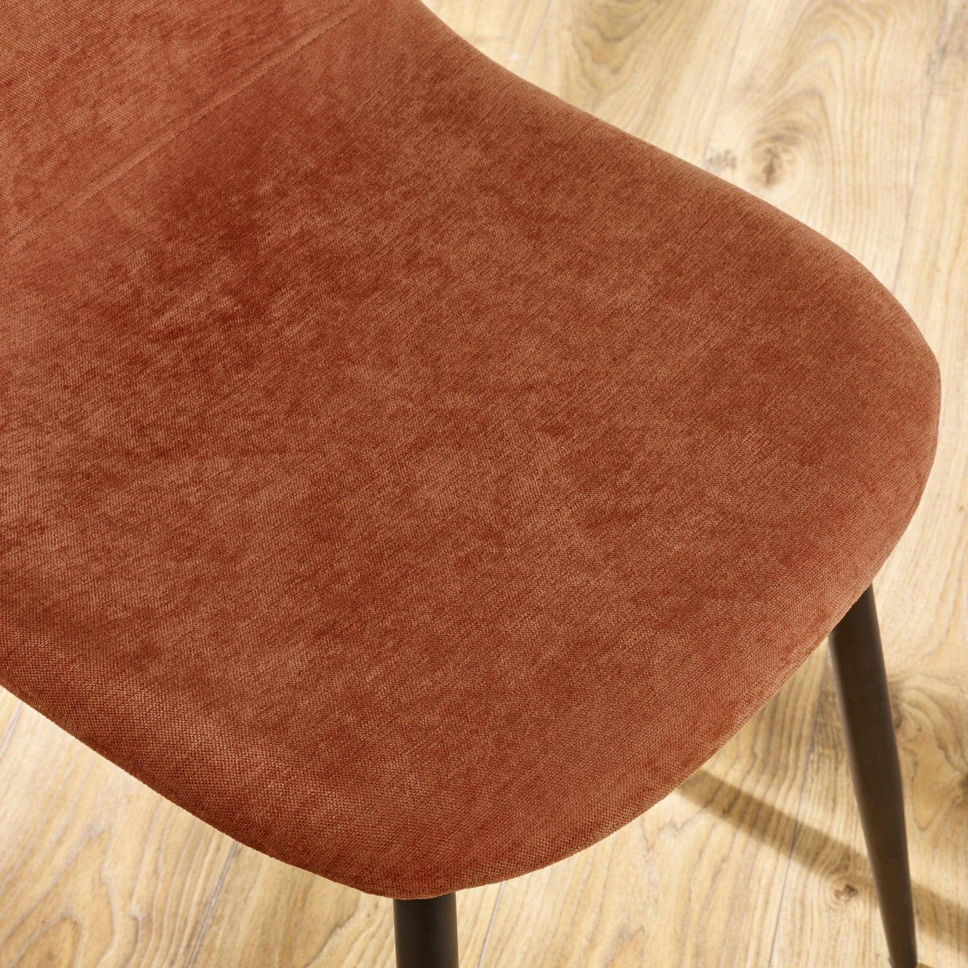 Closeup of rust fabric dining chair seat with black legs on light wood floor