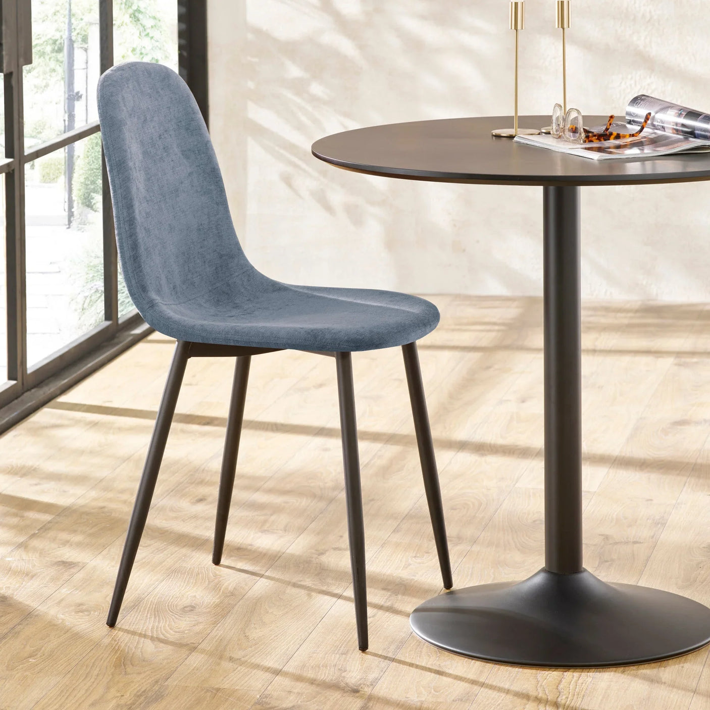 Grey fabric dining chair with black metal legs next to round dining table on wood floor