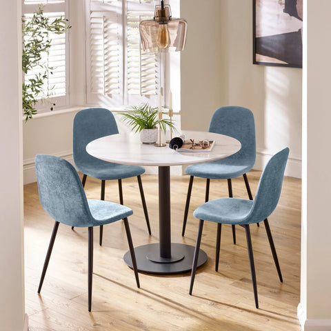 Round dining table with white top and four blue velvet dining chairs on wood floor