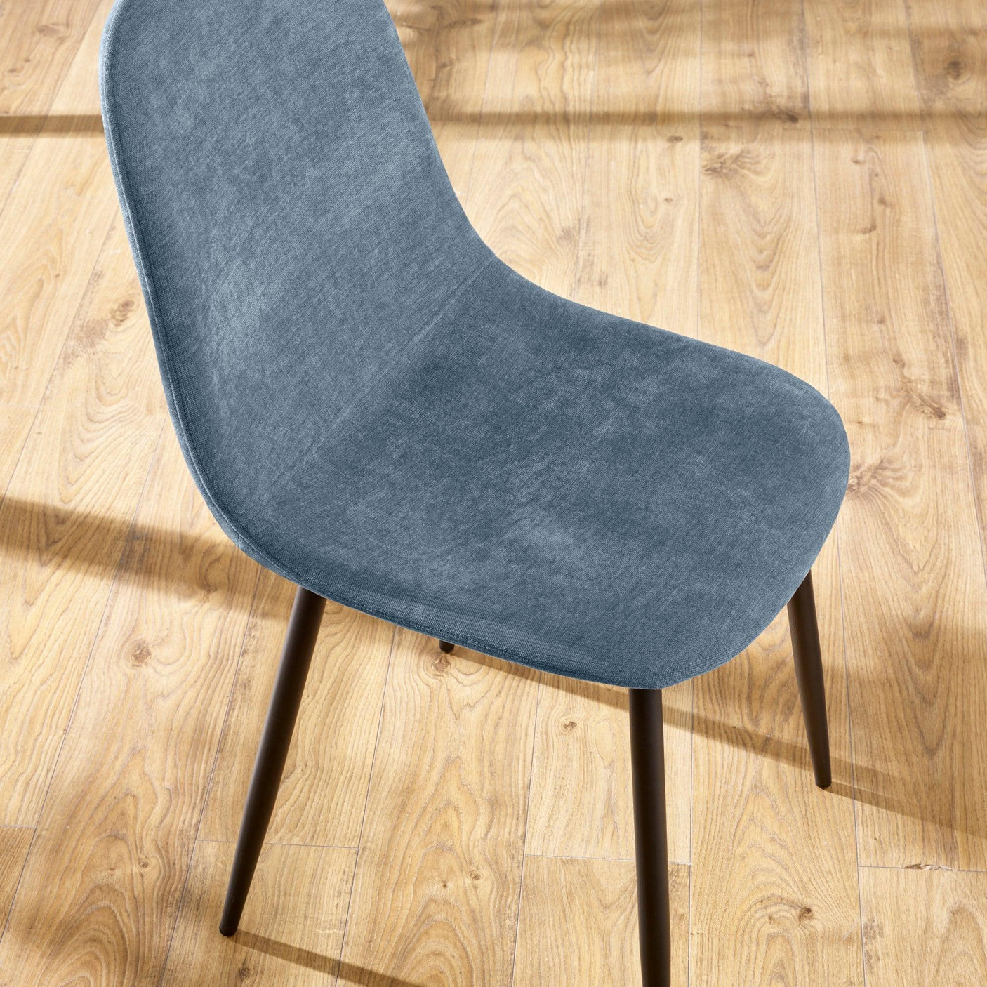 Blue fabric dining chair with curved seat and black legs on wooden flooring