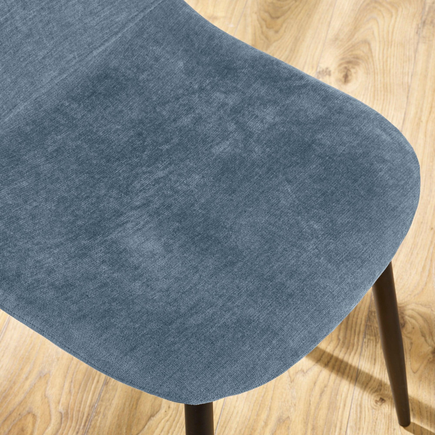 Blue fabric dining chair seat with black legs on light wood floor