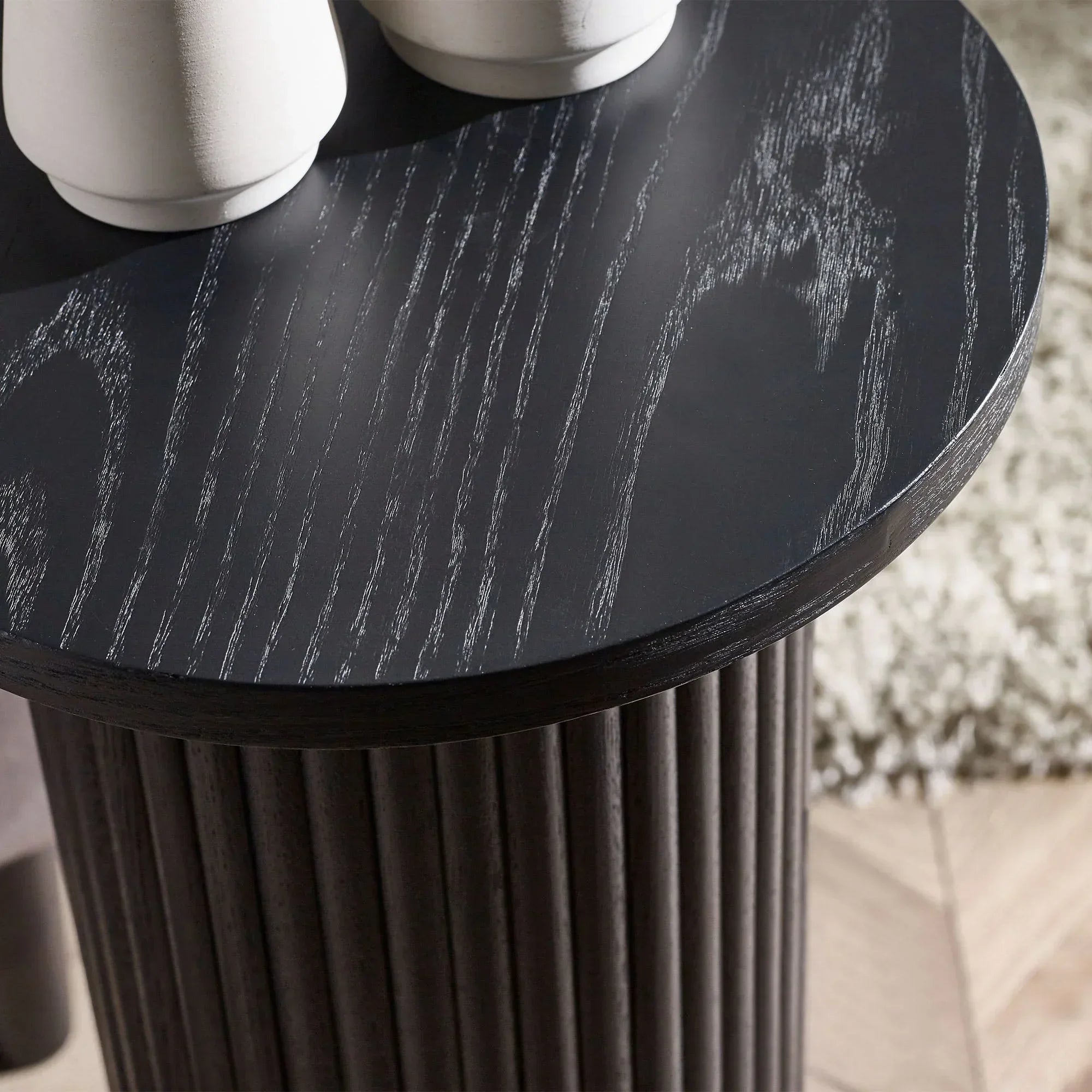 Black fluted drinks table with wood grain detail and round top, closeup view