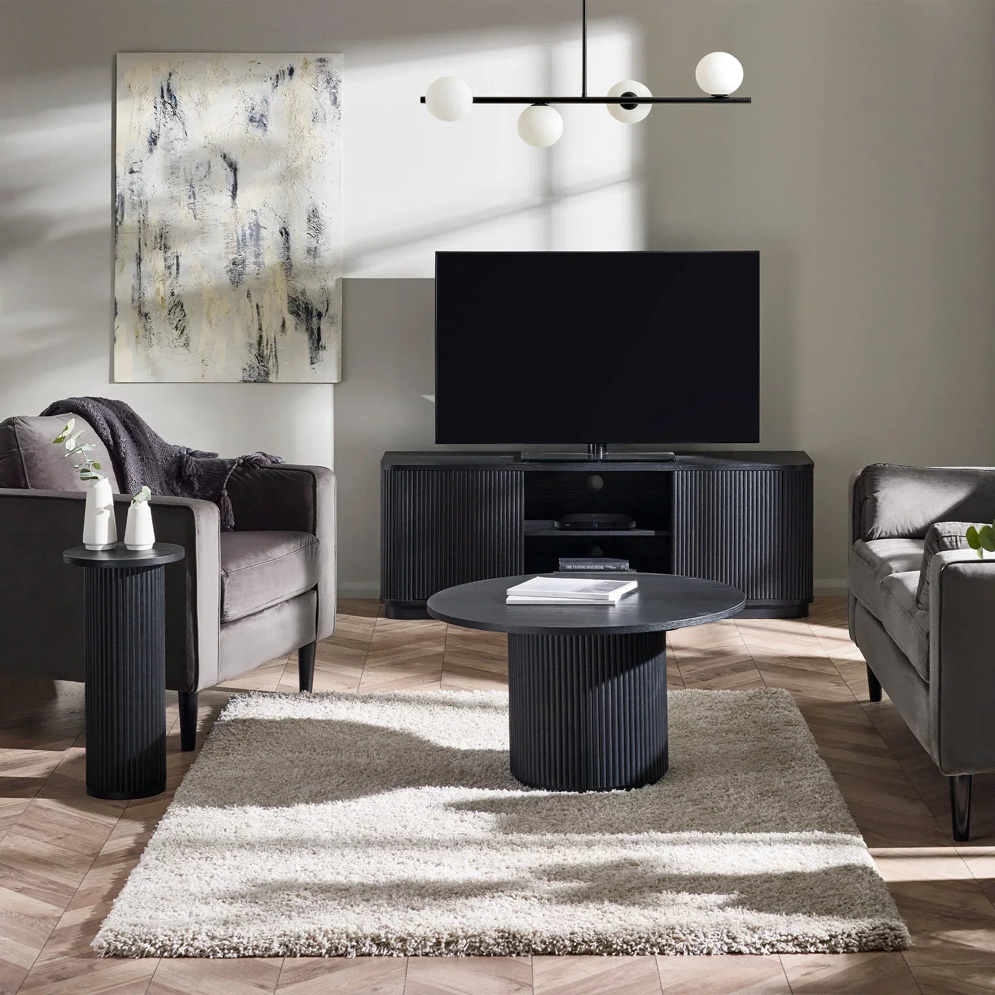 Black fluted drinks table beside grey armchair in modern living room with TV and neutral decor