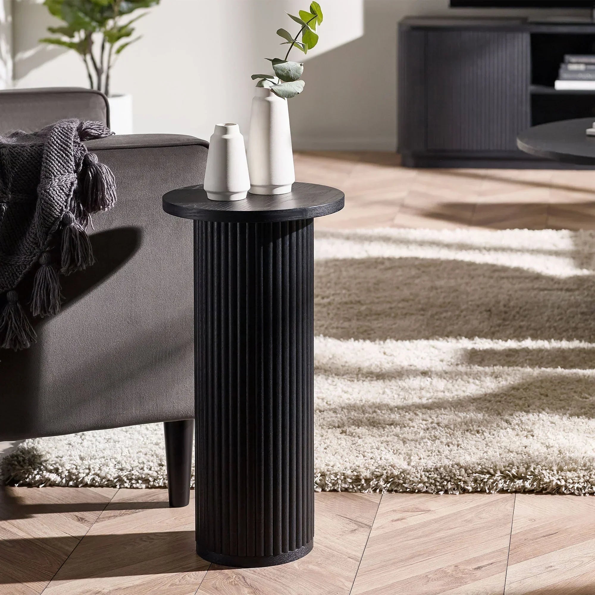 Black fluted drinks table beside sofa with white vases in modern living room