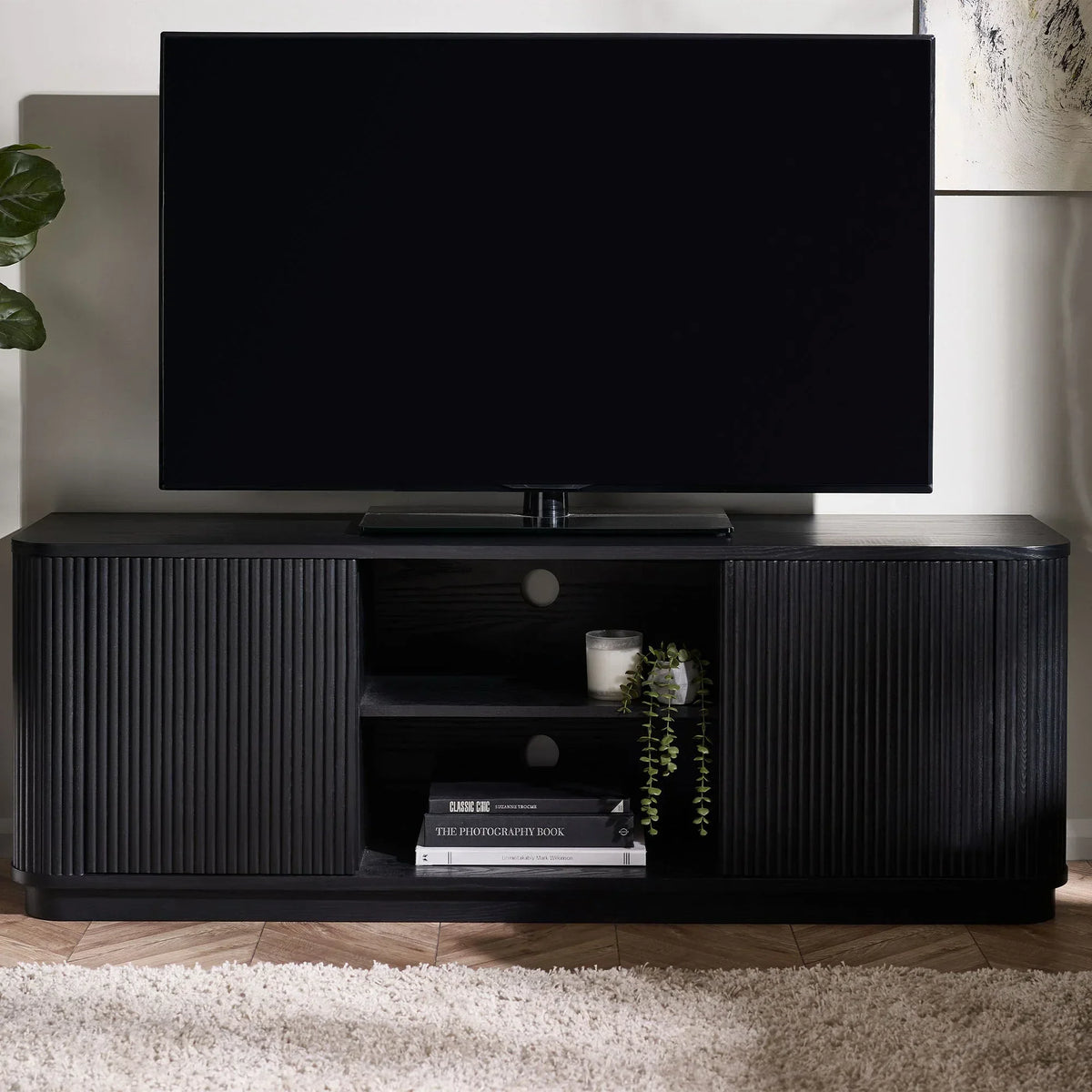 Black fluted TV unit with open shelving, books, candle, and a TV on top in a living room