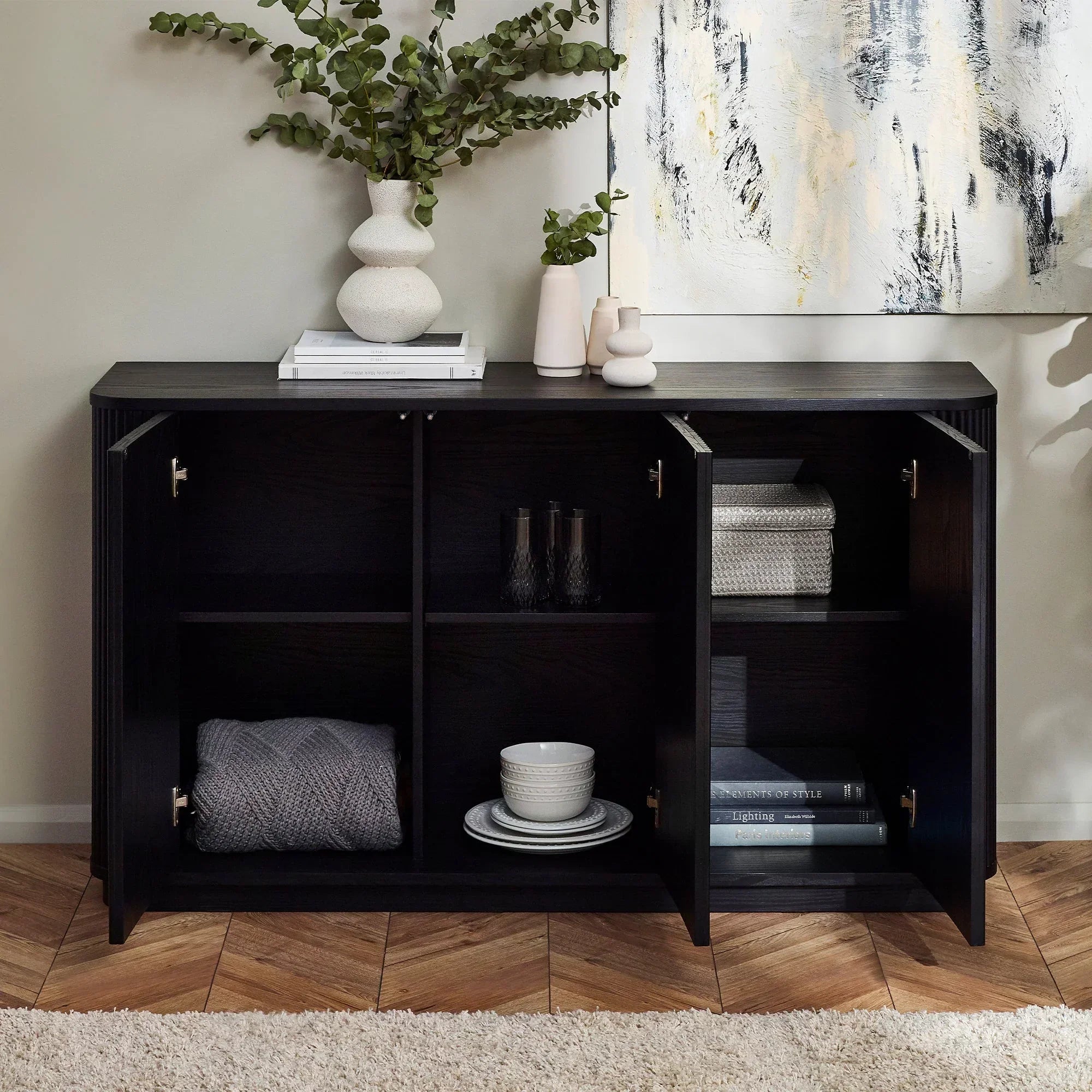 Black fluted sideboard with open doors, shelves holding dishes, books, and vases on top