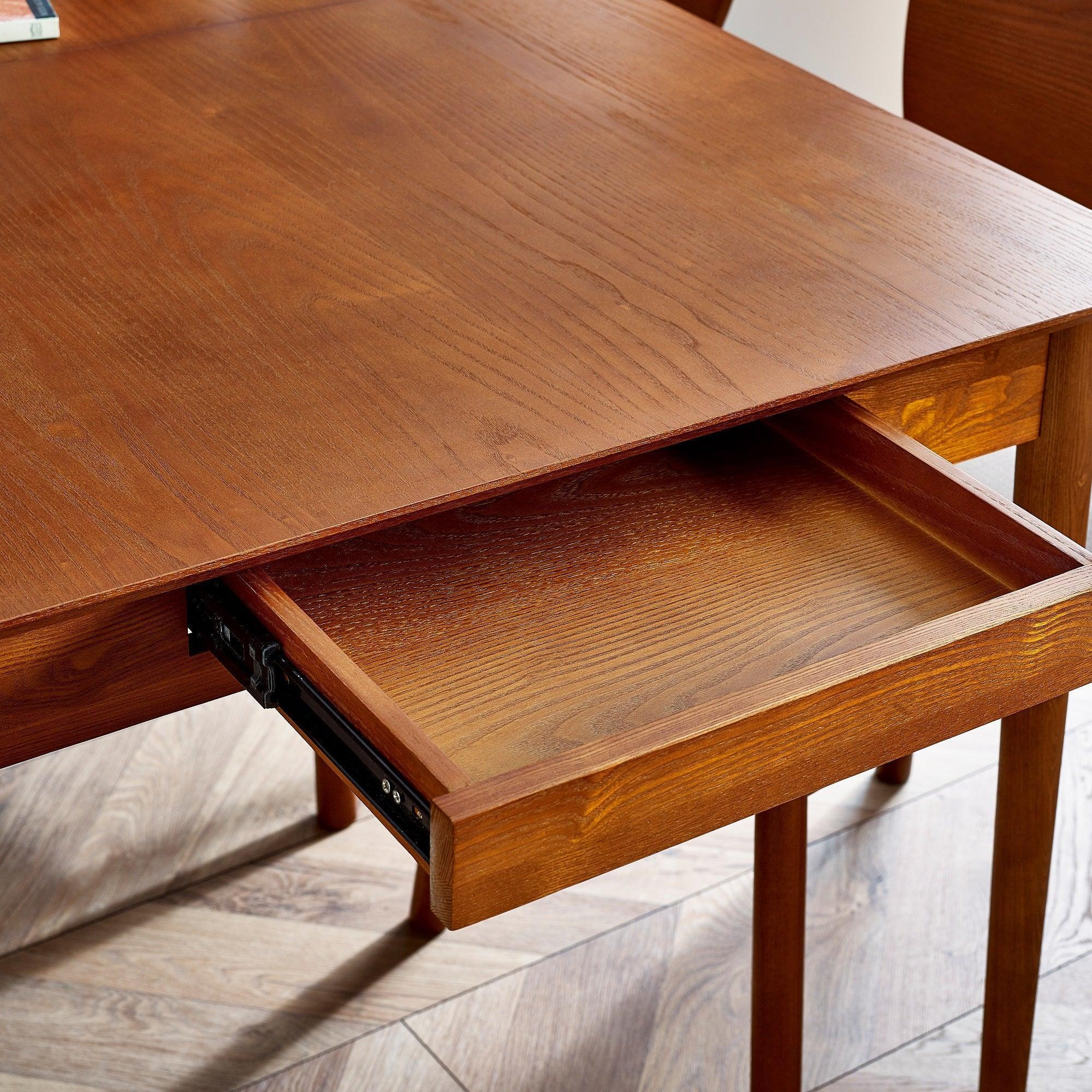 Extendable wooden dining table with pull-out drawer on oak floor