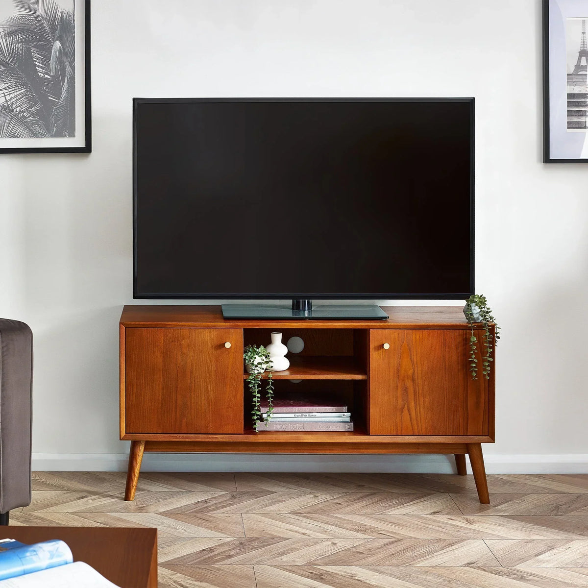 Walnut media unit with two doors, open shelf, TV on top, and decorative plants