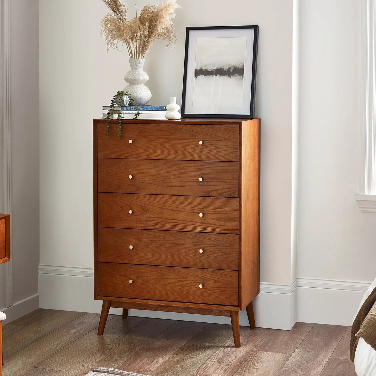Mid-century wooden 5 drawer chest with brass knobs in a bedroom corner, decorated with vases