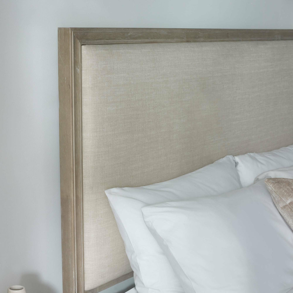 Close up of double bed with beige fabric headboard and white pillows