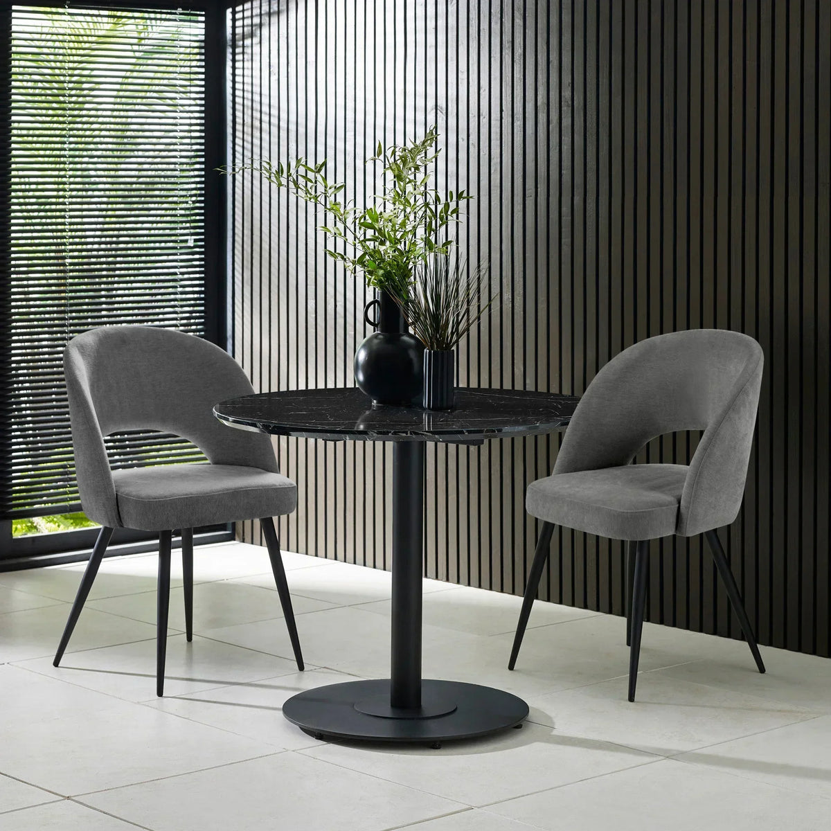 Round black dining table with marble top and two grey upholstered chairs in modern room