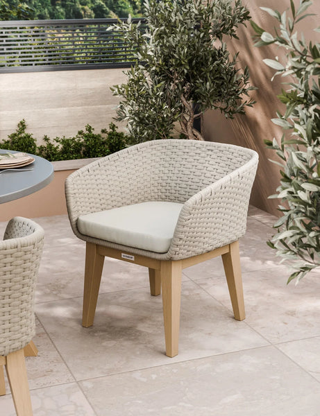 Beige woven outdoor dining chair with cushion on patio near greenery