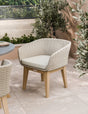 Beige woven outdoor dining chair with cushion on patio near greenery