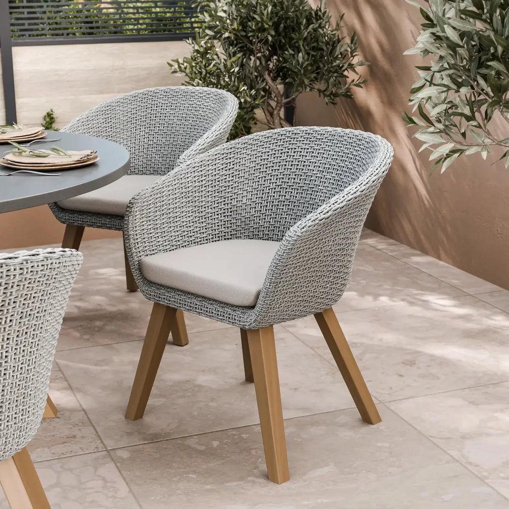 Grey woven outdoor dining chair with beige cushion and wooden legs on tiled patio