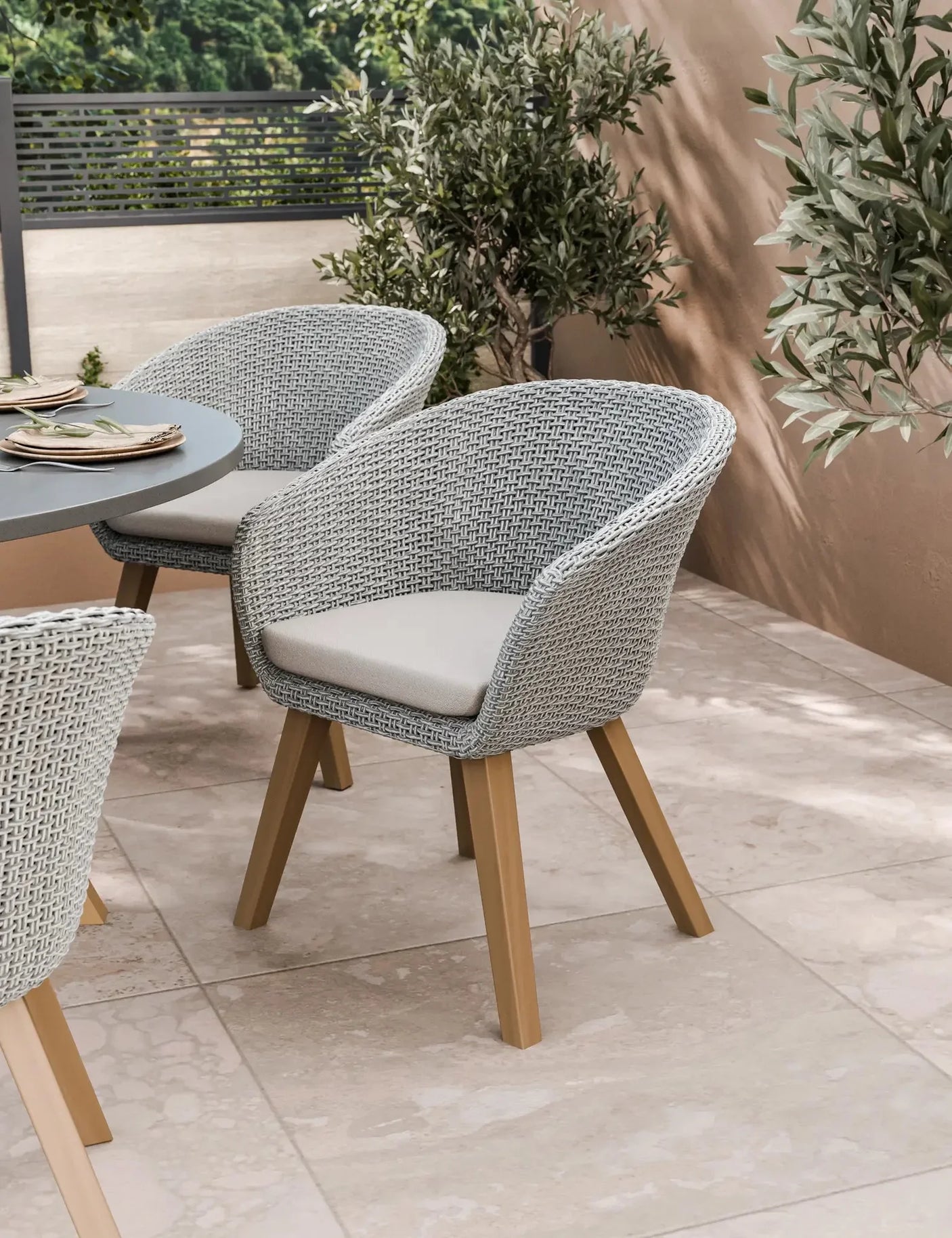 Grey woven outdoor dining chair with beige cushion and wooden legs on tiled patio