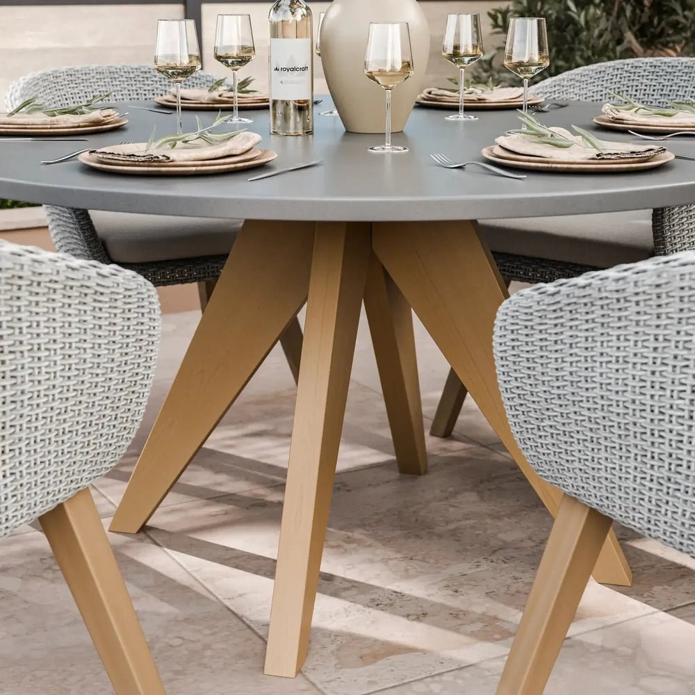 Round outdoor dining table with grey top, wooden legs, and woven armchairs set for four