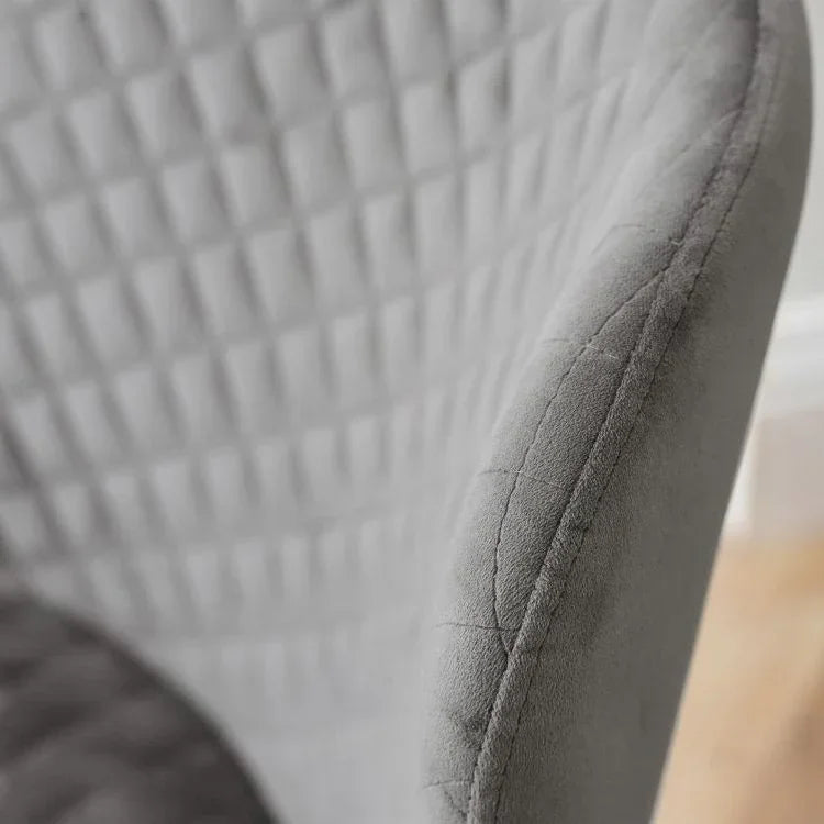 Close-up of grey upholstered chair with diamond-quilted fabric and curved backrest