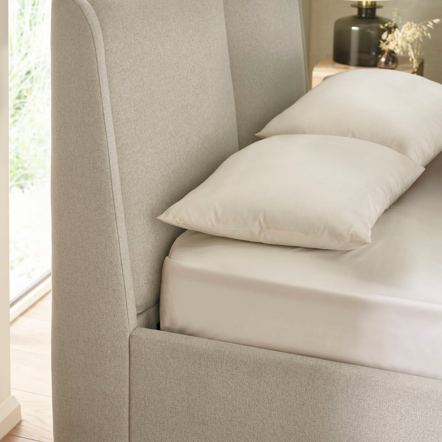 Side view of beige fabric upholstered bed headboard with white pillows and bedding