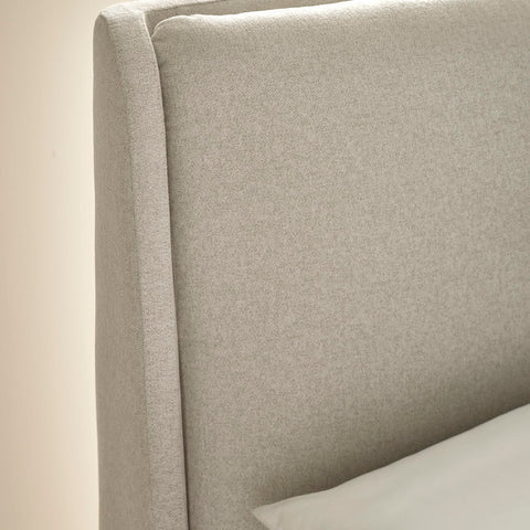 Close-up of beige fabric headboard with seam detail and white pillow