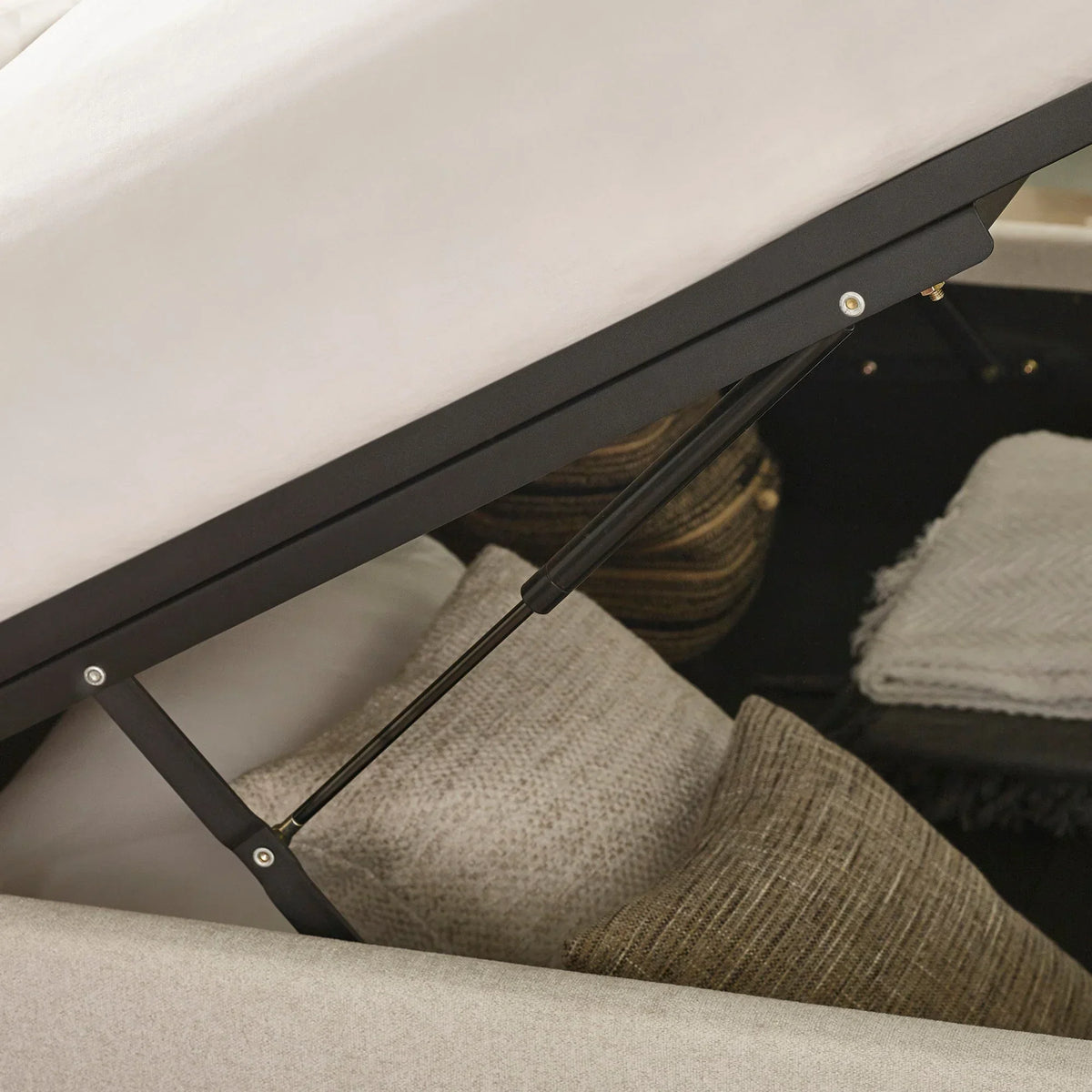 Ottoman storage bed mechanism with cushions and grey throw blankets inside compartment