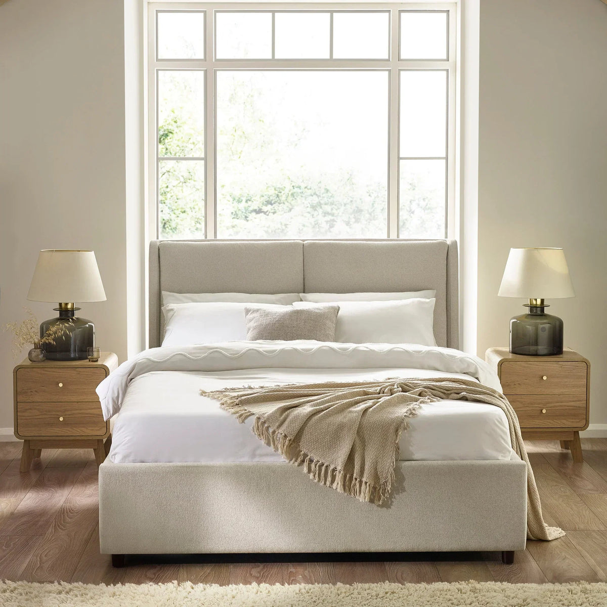 Cream upholstered bed with headboard, white bedding, throw, wooden bedside tables and lamps