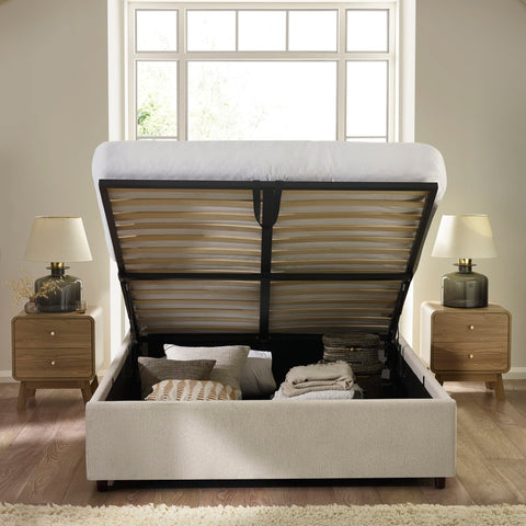 Beige upholstered lift-up storage bed open revealing storage space filled with pillows and blankets
