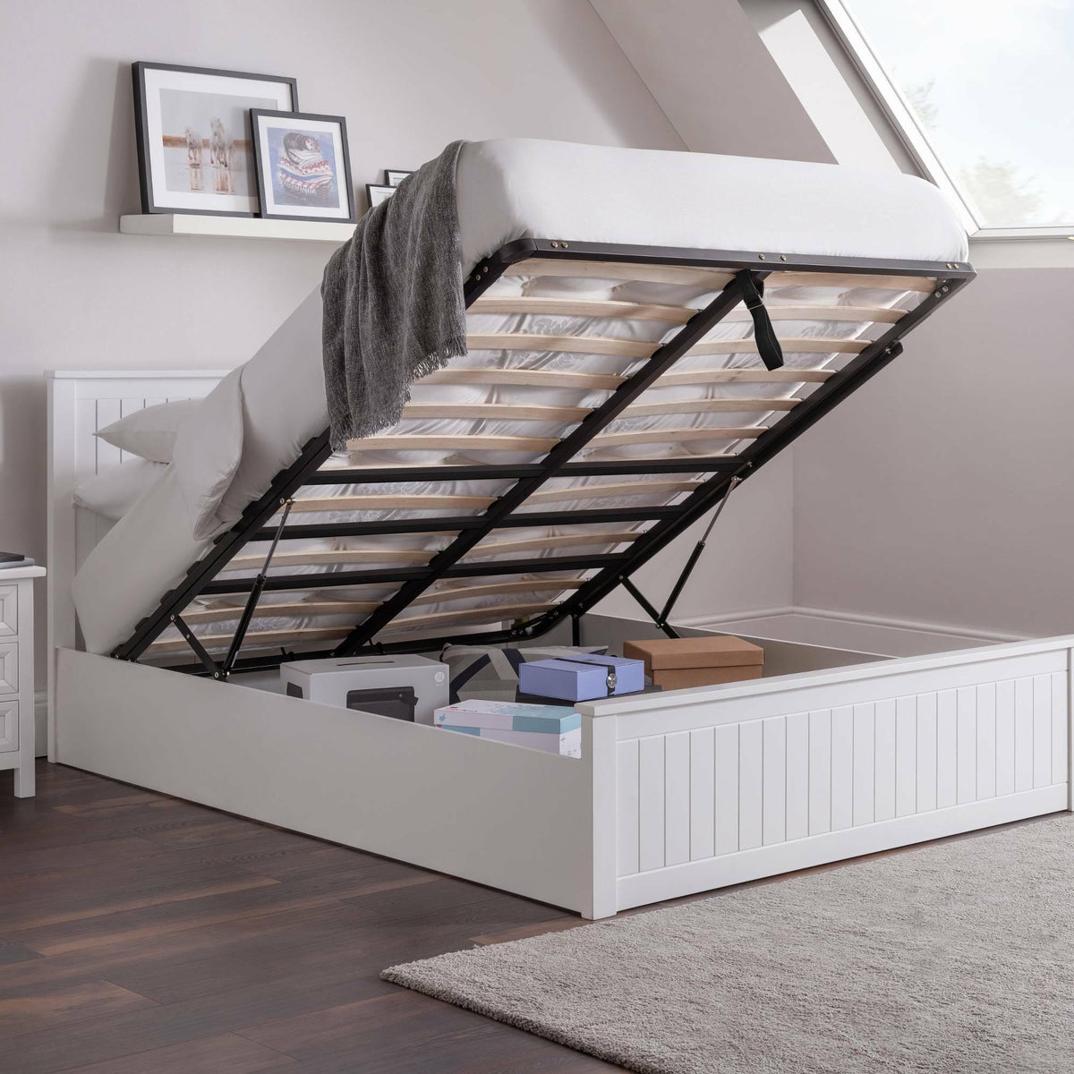 White ottoman storage bed with lifted base showing boxes and folded blanket inside