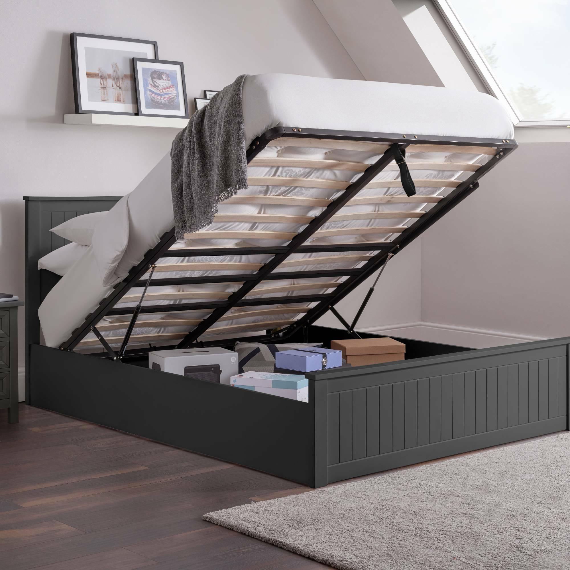 Dark grey ottoman storage bed with raised mattress base, boxes stored underneath, bedroom setting