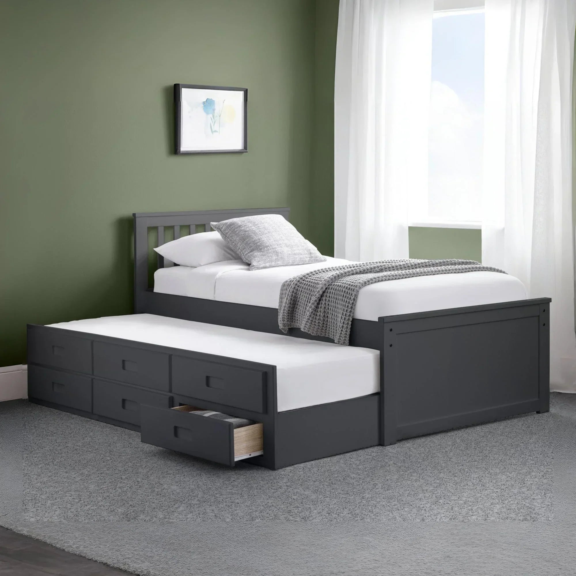 Grey wooden single bed with pull out trundle and storage drawers, set against green wall