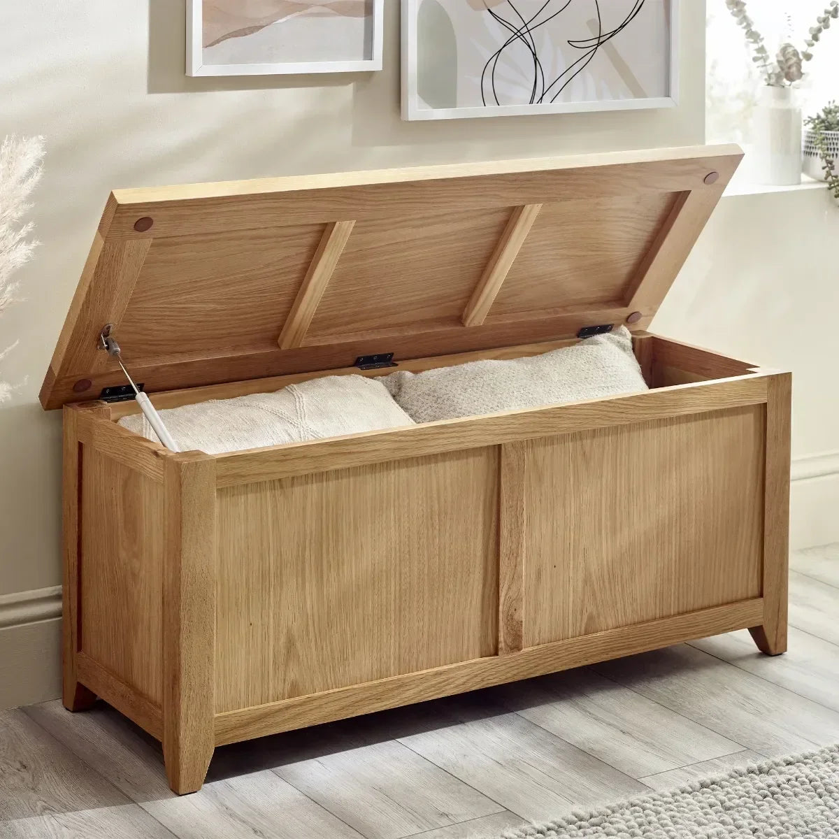 Oak storage chest with lid open, showing pillows inside, positioned on wooden floor