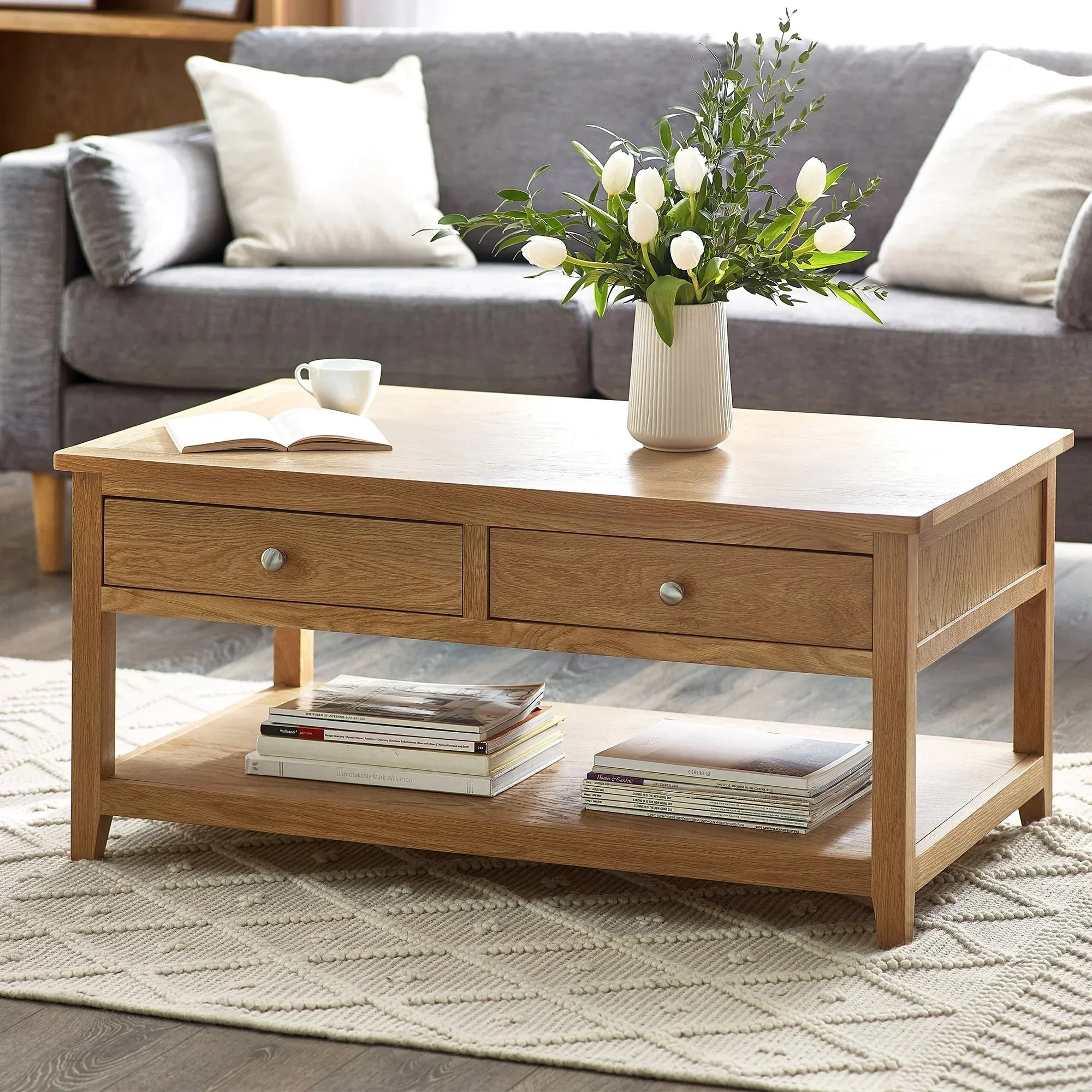 Oak coffee table with two drawers, vase of tulips, books on shelf, in living room setting