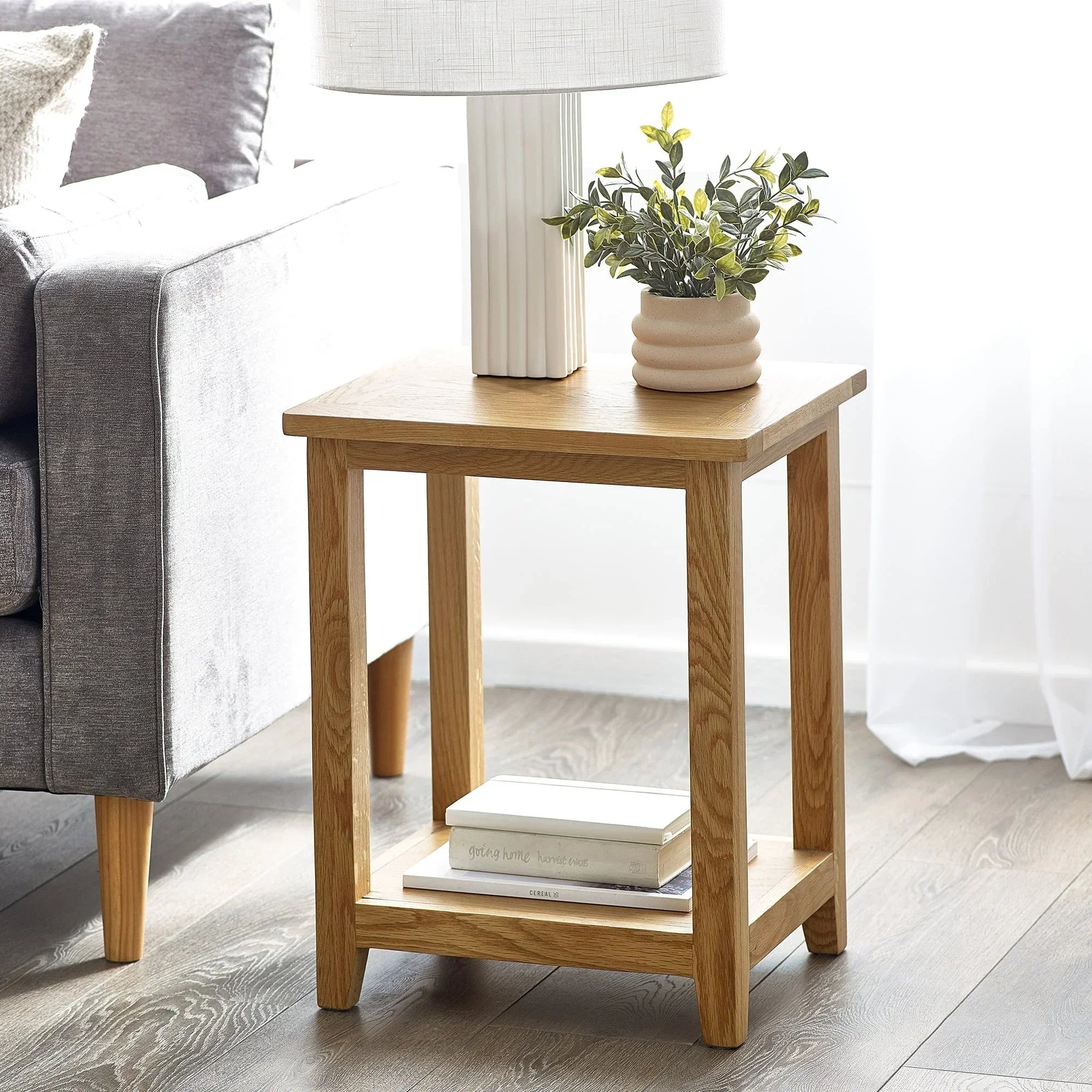 Oak lamp table with lower shelf, styled with plant and books in living room setting