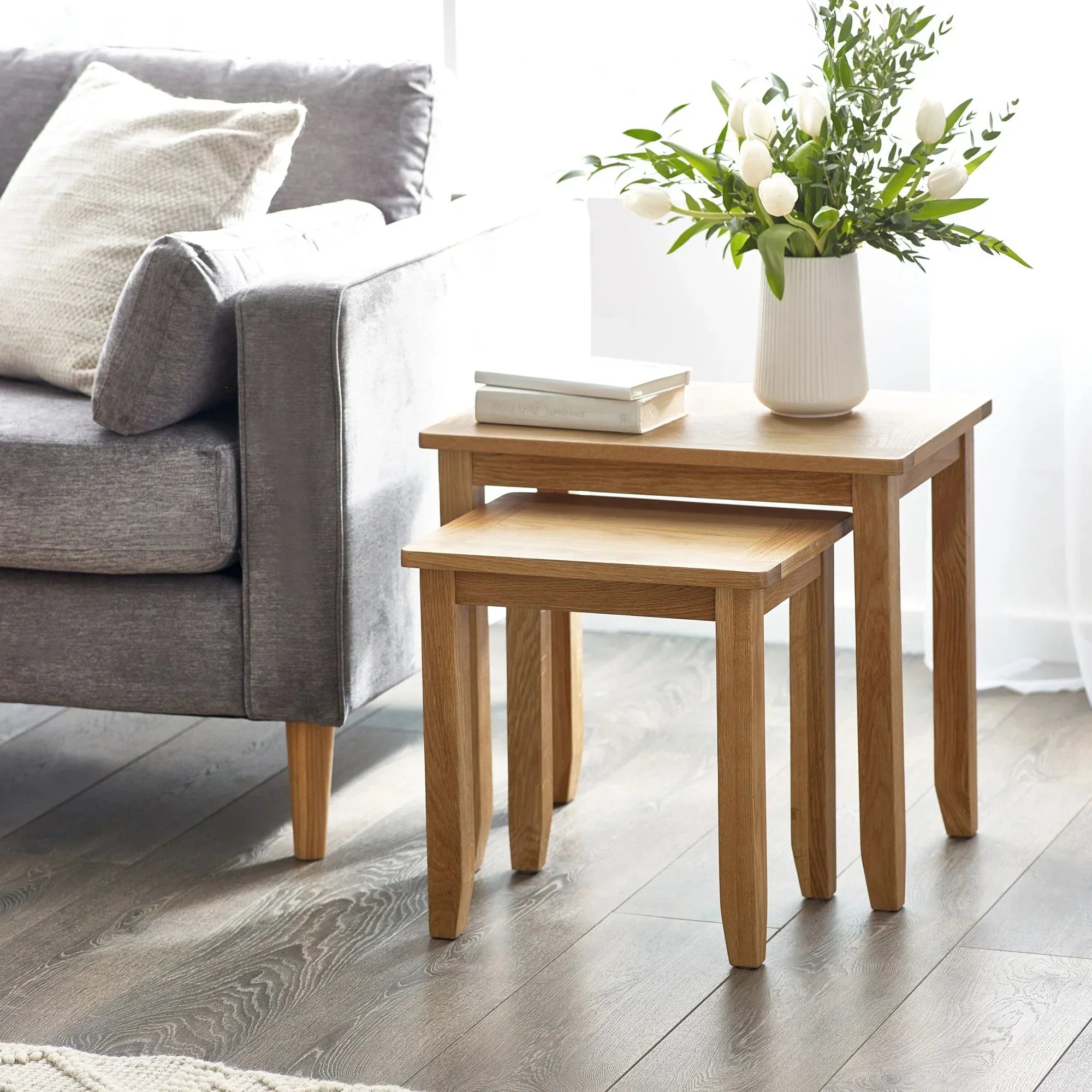 Oak nest of tables set beside grey sofa with vase of flowers and books on top table