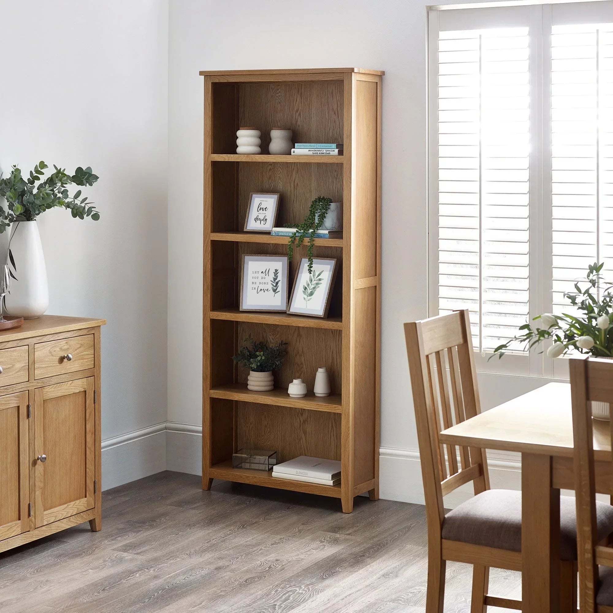 Tall oak bookcase with shelves styled with decor, plants, and books in dining room