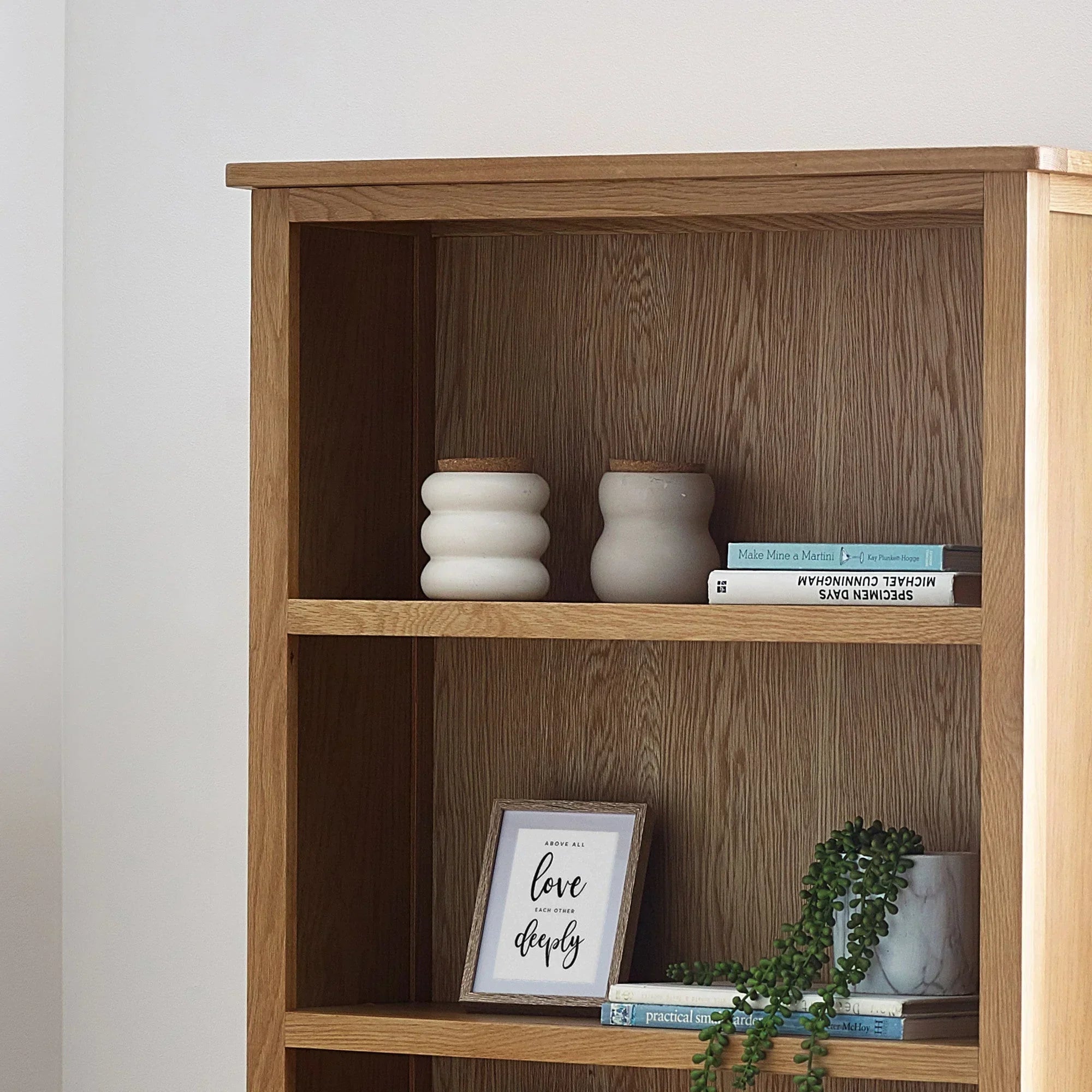 Oak tall bookcase shelves styled with books, framed print, vases, and small plant
