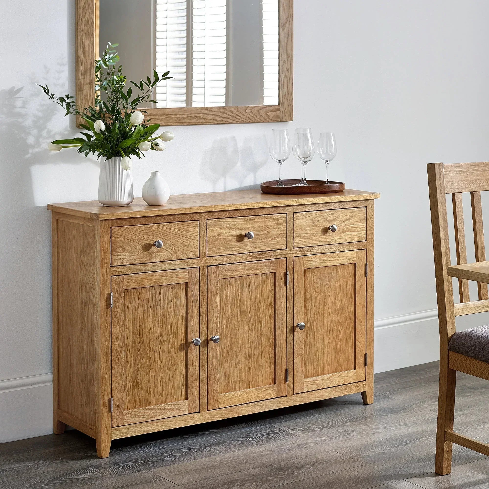 Oak sideboard with three drawers and four doors in dining room, decorated with vases and glasses