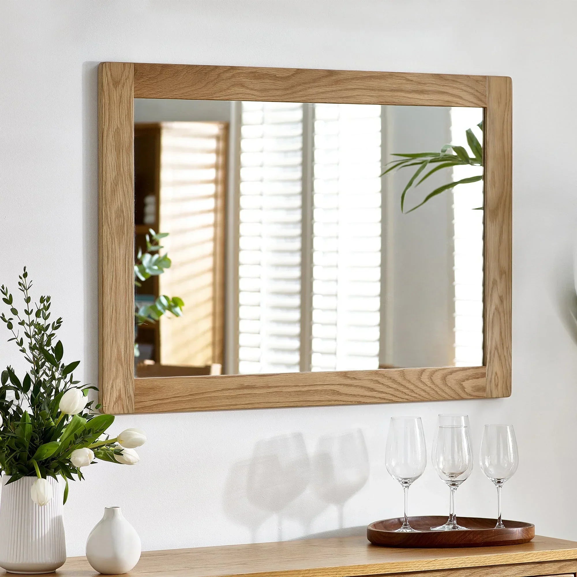 Rectangular wall mirror with natural wood frame above sideboard, vase and glassware visible