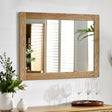 Rectangular wall mirror with natural wood frame above sideboard, vase and glassware visible