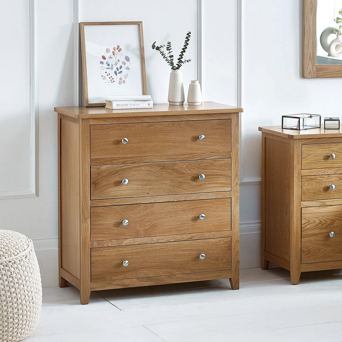 Oak 4 drawer chest with silver knobs in bright bedroom, styled with framed print and vases