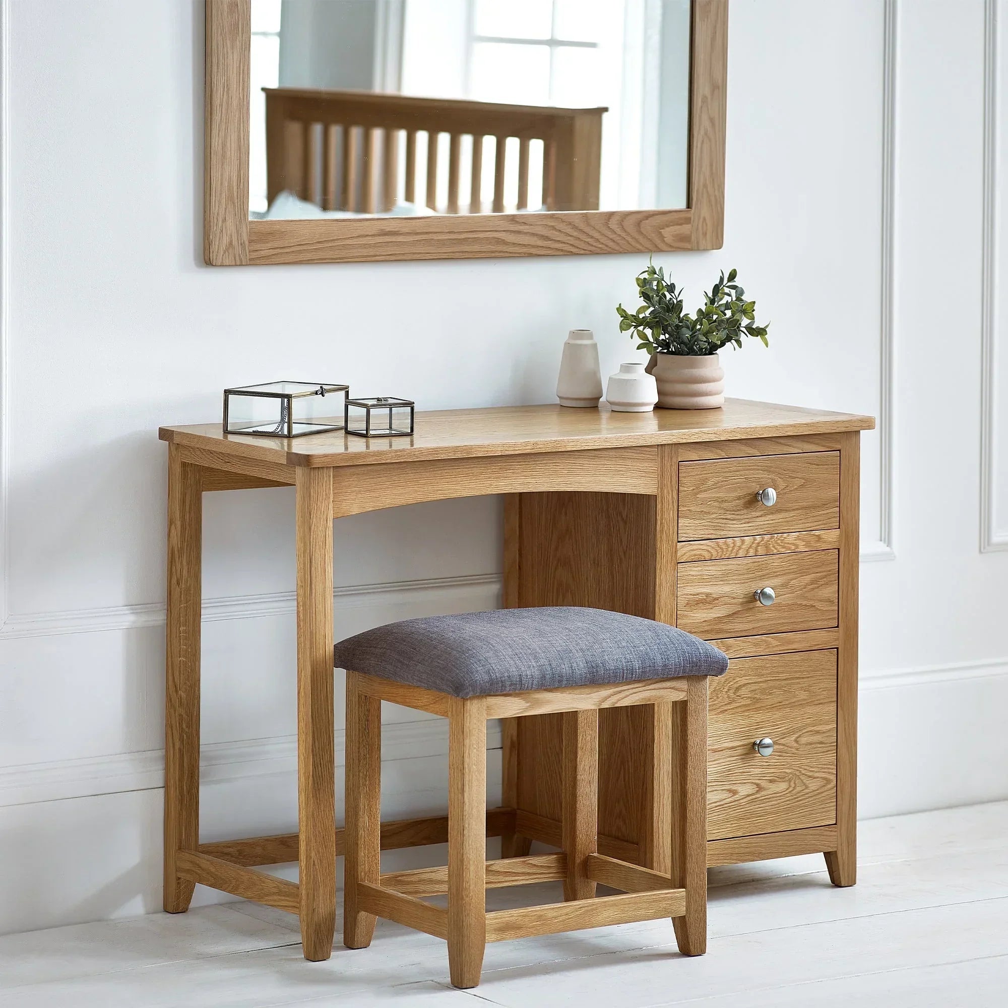 Oak dressing table with three drawers and grey cushioned stool in a bright bedroom