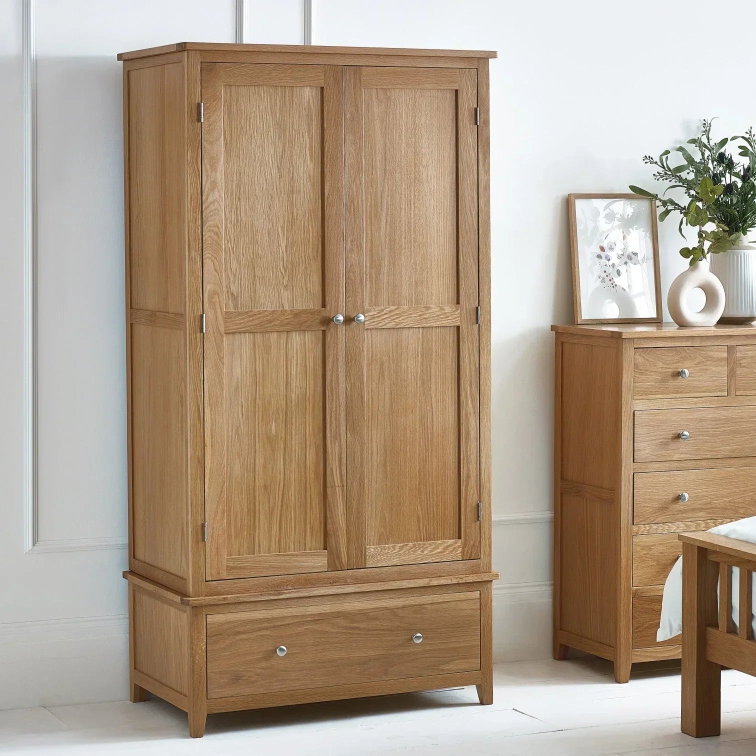 Oak combination wardrobe with drawer shown in a bright bedroom beside matching chest of drawers