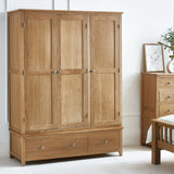 Oak 3 door wardrobe with panelled doors and two drawers in a bright bedroom