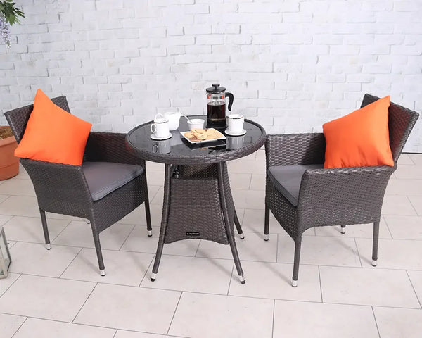 Two seater rattan bistro set with round glass top table, orange cushions, and grey seats